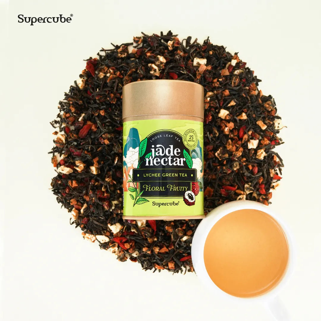 Supercube Jade Nectar Lychee Green Tea tin on a bed of loose leaf tea with a cup of brewed tea