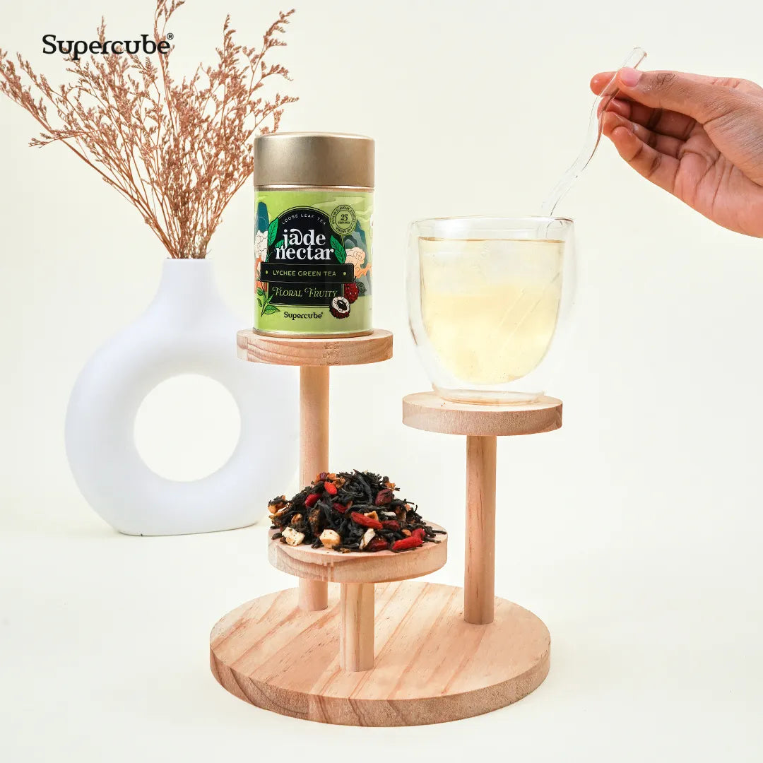 Supercube Jade Nectar Lychee Green Tea tin on a wooden display with loose leaf tea and a glass of brewed tea