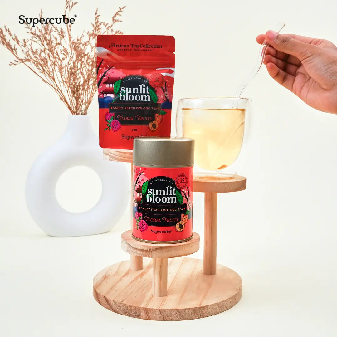Supercube Sweet Peach Oolong tin and refill pouch on a wooden display with a glass of brewed oolong tea