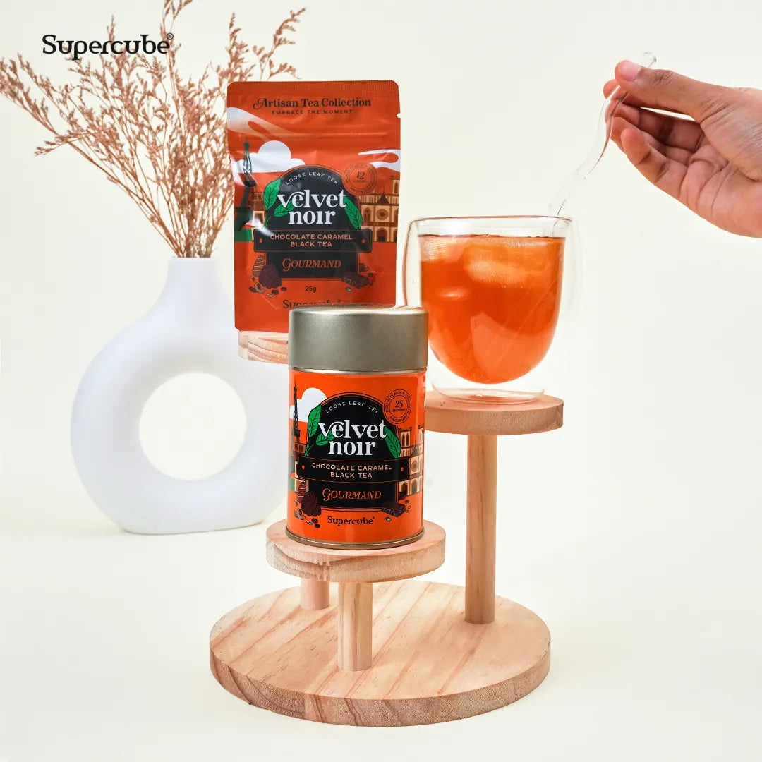 Supercube Velvet Noir Chocolate Caramel Black Tea tin and refill pouch on a wooden display with a glass of iced tea